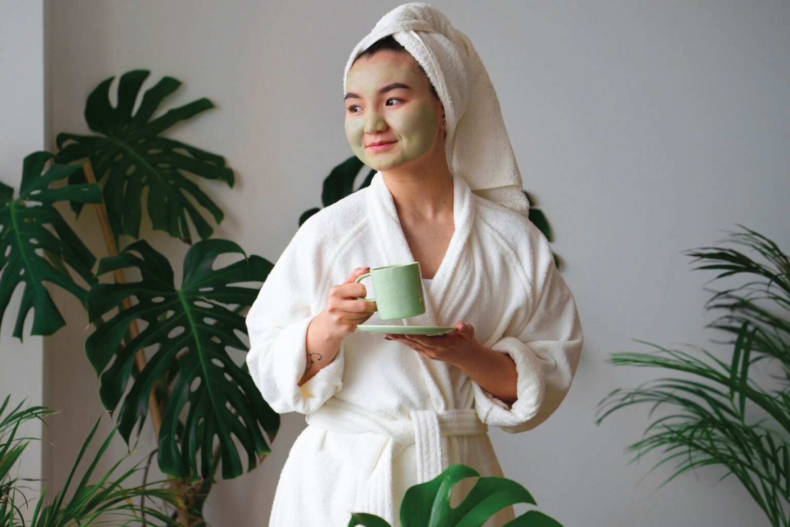 Woman with a green clay facial mask relaxing among houseplants